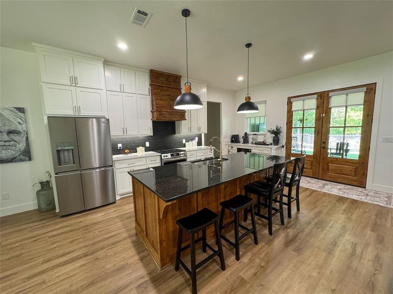 Kitchen featuring appliances with stainless steel finishes, decorative backsplash, white cabinets, dark stone countertops, and hanging light fixtures Kitchen featuring appliances with stainless steel finishes, decorative backsplash, white cabinets, dark stone countertops, and hanging light fixtures