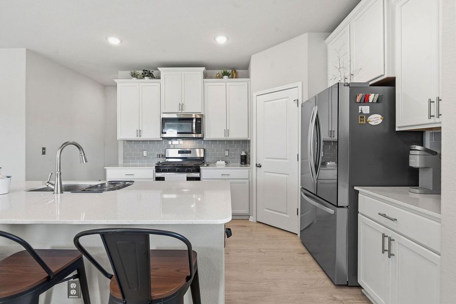 Kitchen featuring a breakfast bar area, stainless steel appliances, white cabinets, light wood-type flooring, and recessed lighting Kitchen featuring a breakfast bar area, stainless steel appliances, white cabinets, light wood-type flooring, and recessed lighting