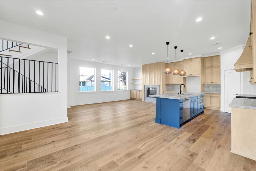 Second-floor main living and kitchen area with abundant natural light, high ceilings, engineered wood floors, custom built-ins, and a stunning custom fireplace as the focal point. Features an oversized island with Taj Mahal quartzite countertops and integrated appliances.