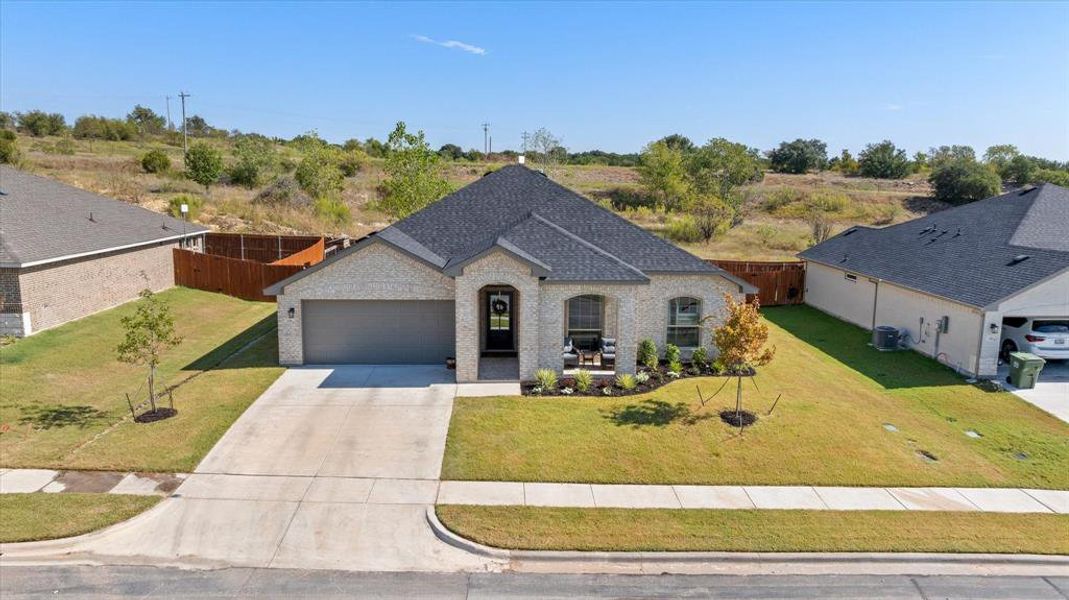 French country inspired facade with brick siding, concrete driveway, a shingled roof, and an attached garage