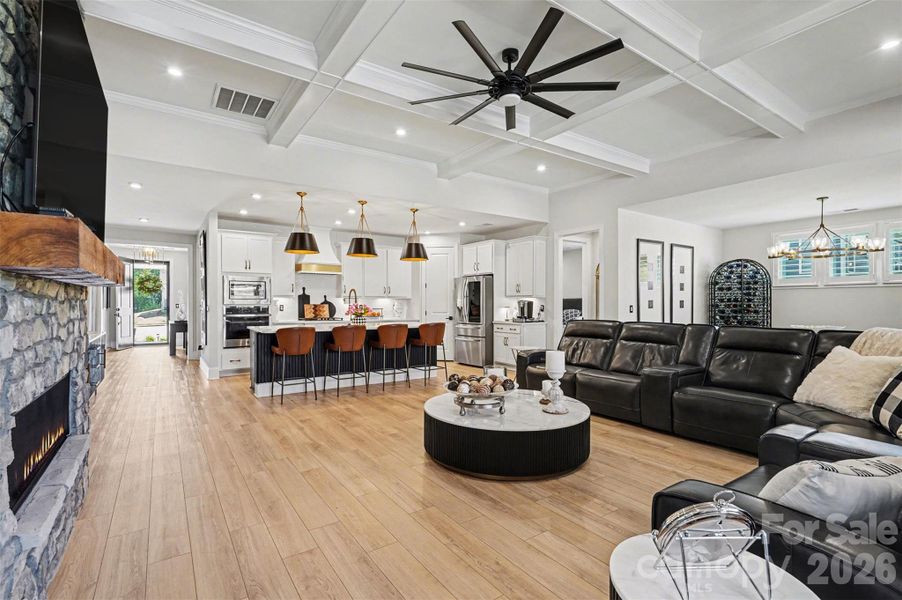 This expansive great room seamlessly blends a cozy living area anchored by a floor-to-ceiling stone fireplace with a gourmet kitchen featuring a sleek black island, and elegant pendant lighting.