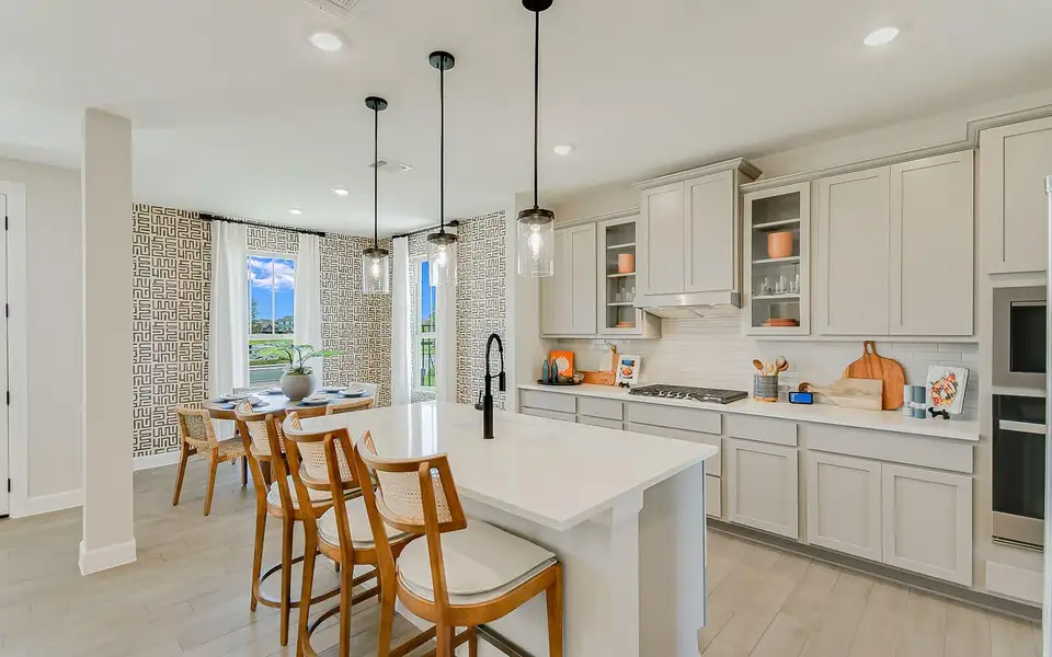 Kitchen with a breakfast bar area, glass fronted cabinets, light wood finished floors, a kitchen island with sink, and pendant lighting
