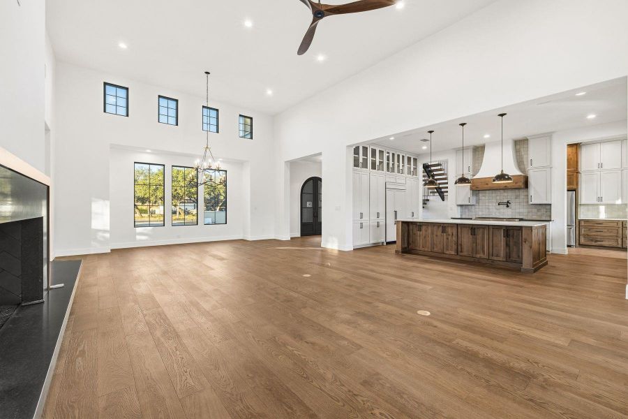 Unfurnished living room with ceiling fan, dark wood-style floors, a high ceiling, arched walkways, and suspended lighting