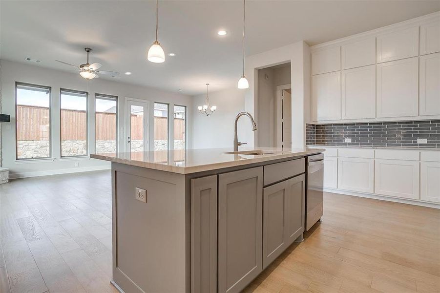 Kitchen with light wood-type flooring, tasteful backsplash, an island with sink, and plenty of natural light