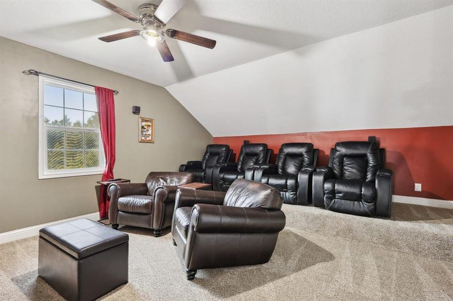 Cinema room featuring ceiling fan, carpet flooring, and vaulted ceiling