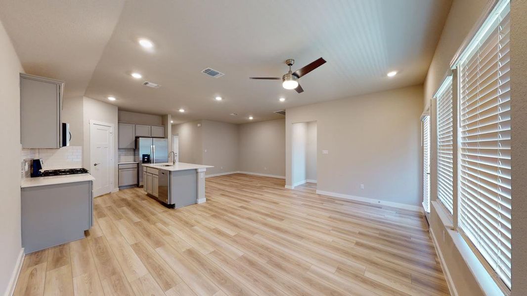 Kitchen featuring gray cabinets, open floor plan, ceiling fan, an island with sink, and light wood finished floors