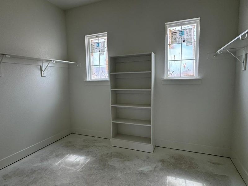 Room featuring two windows, a built-in shelving unit, and perimeter shelving with hanging rods