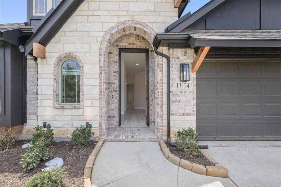 Home entrance with arched brick doorway, stone exterior, and concrete walkway leading to open front door