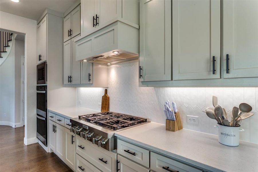 Kitchen with appliances with stainless steel finishes, light stone countertops, decorative backsplash, and dark wood-style flooring Kitchen with appliances with stainless steel finishes, light stone countertops, decorative backsplash, and dark wood-style flooring