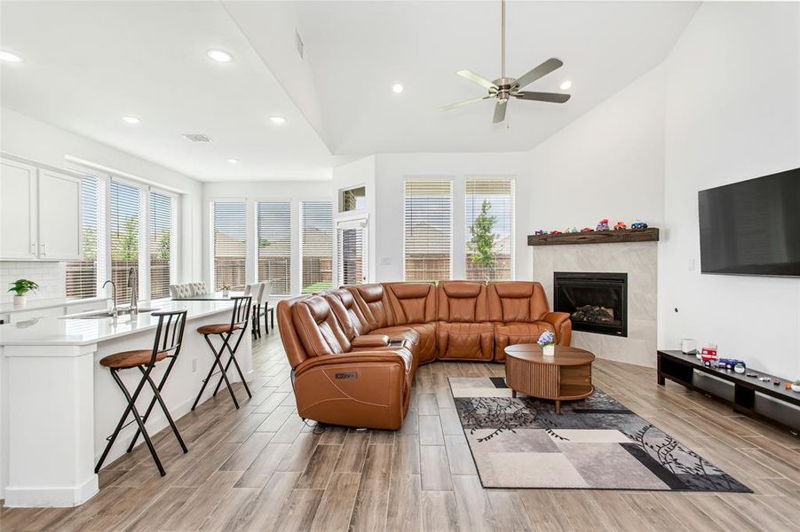 Vaulted ceiling living area featuring a fireplace with a wood mantel, tile surround, and an integrated ceiling fan