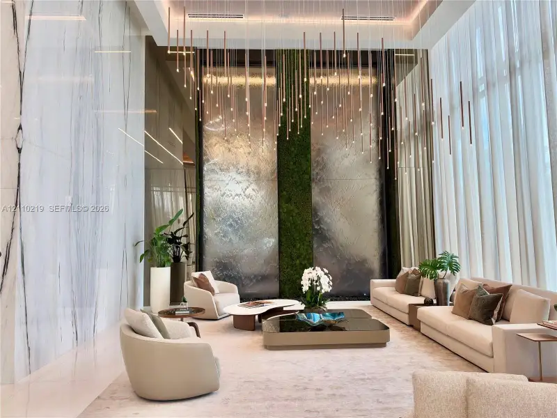 Double-height ceilings featuring a multi-pendant light installation, floor-to-ceiling stone wall cladding, and a dual-panel indoor water feature with vertical moss integration