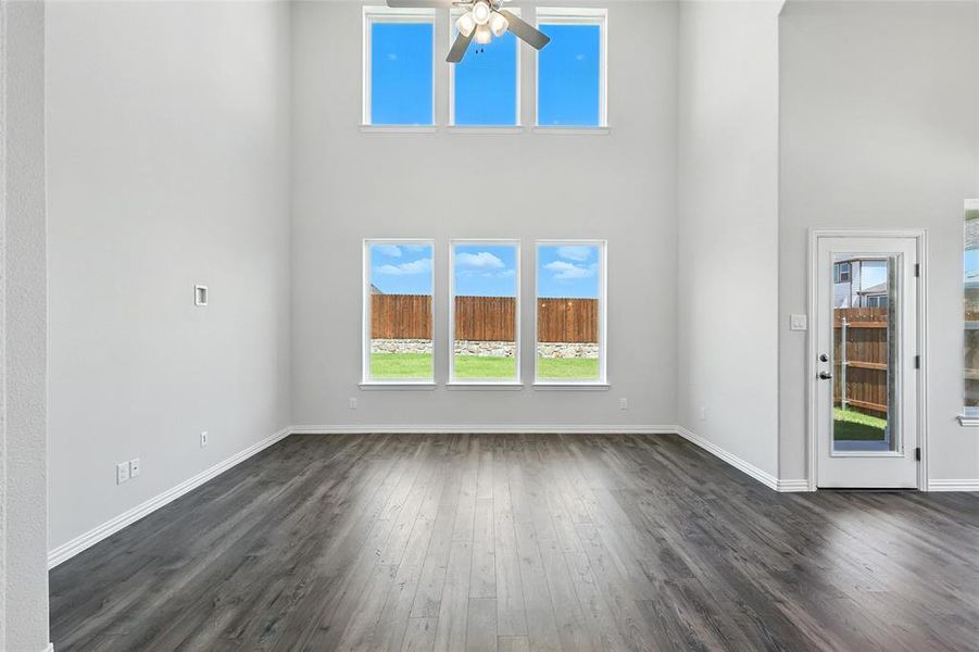 Unfurnished living room featuring ceiling fan, dark wood-style flooring, and a high ceiling