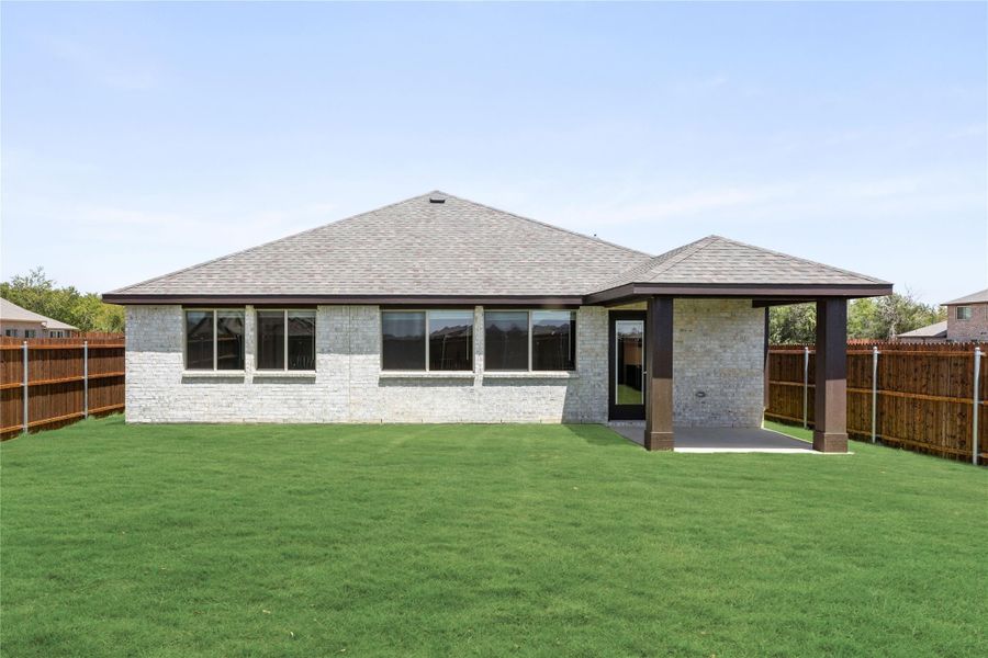 Rear exterior of single-story brick home with covered patio, large windows, and fenced backyard with green lawn