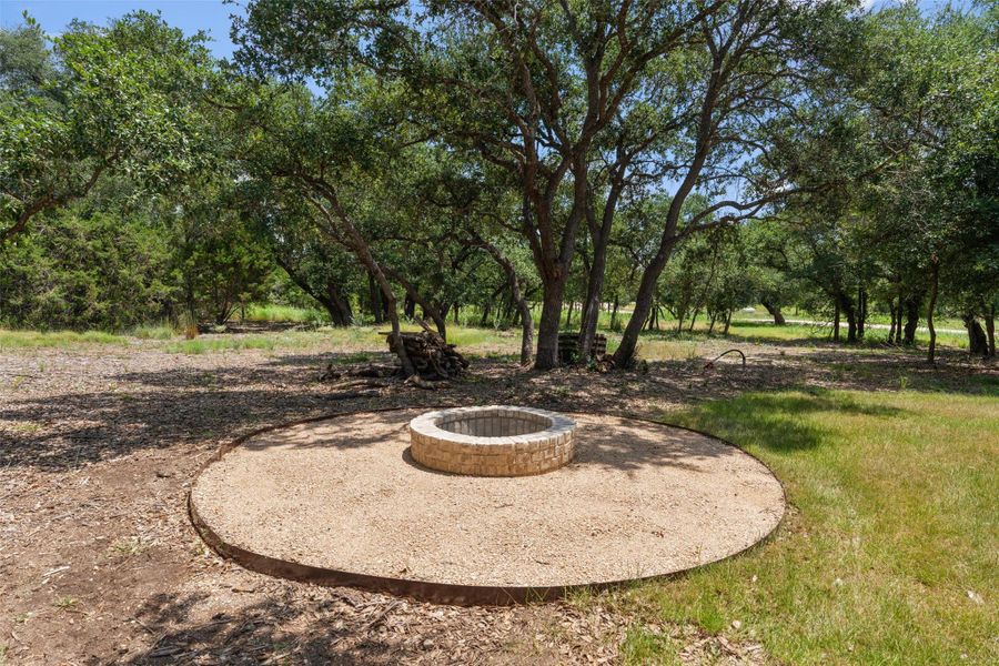 A stone fire pit ring, perfect for gatherings, is nestled in a clearing of mature trees, offering a private outdoor retreat.