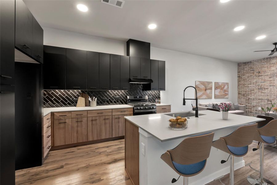 Kitchen featuring stainless steel gas range, a sink, dark cabinetry, under cabinet range hood, and a breakfast bar area