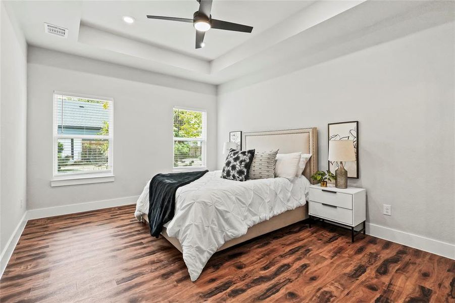 Bedroom with a tray ceiling, dark wood-type flooring, and ceiling fan Bedroom with a tray ceiling, dark wood-type flooring, and ceiling fan