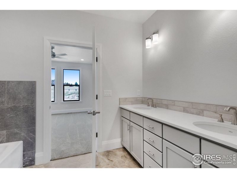 The primary ensuite, featuring dual vanities, a full-width mirror, porcelain tile flooring, and porcelain vanity sinks