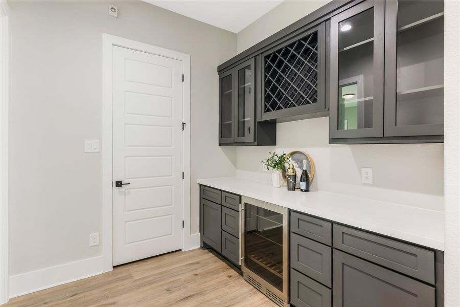 A modern butler's pantry with dark cabinetry, wine rack, and glass-front upper cabinets, and a wine fridge A modern butler's pantry with dark cabinetry, wine rack, and glass-front upper cabinets, and a wine fridge