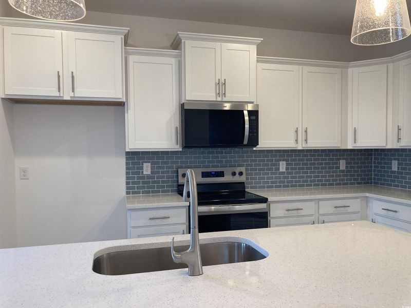 Kitchen featuring pendant lighting, appliances with stainless steel finishes, decorative backsplash, and white cabinetry