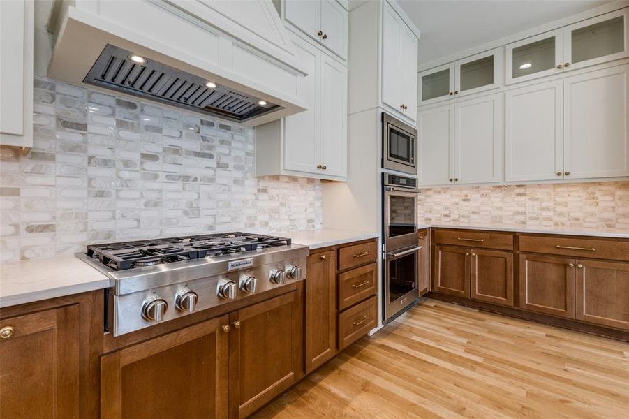 Kitchen with appliances with stainless steel finishes, wall chimney range hood, brown cabinetry, and light countertops