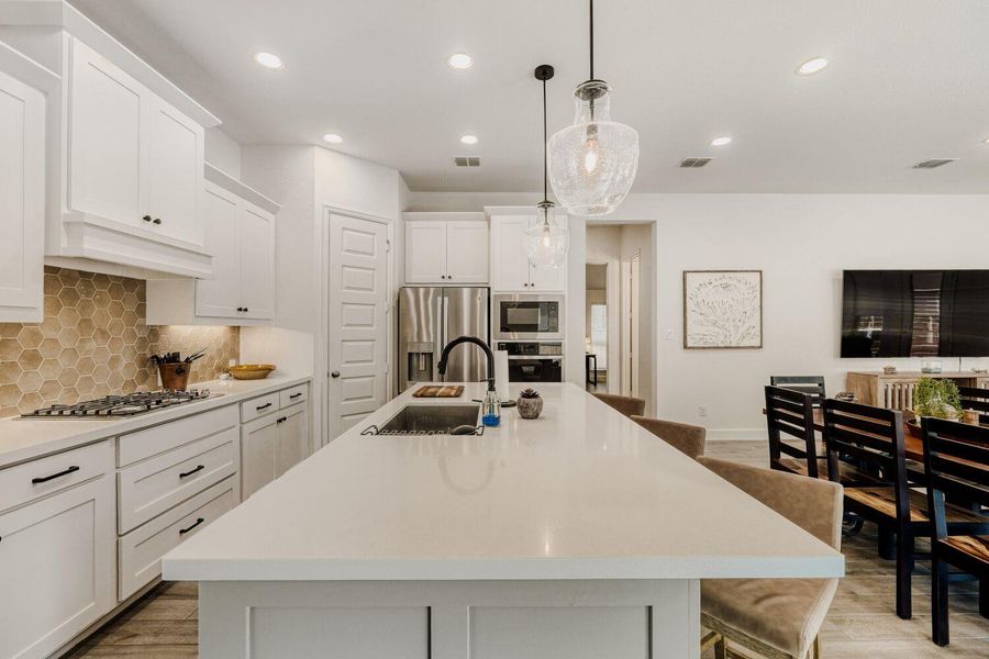 Kitchen with a breakfast bar area, white cabinetry, hanging light fixtures, a center island with sink, and stainless steel appliances