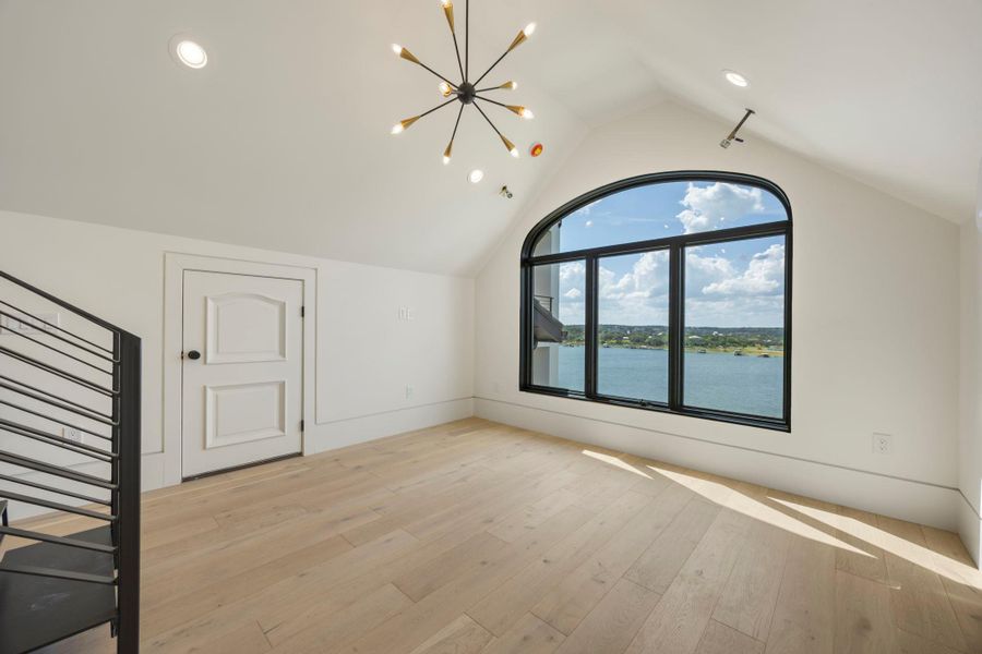 A top-floor bonus room with soaring vaulted ceilings and an expansive lake view from a large arched window. A top-floor bonus room with soaring vaulted ceilings and an expansive lake view from a large arched window.