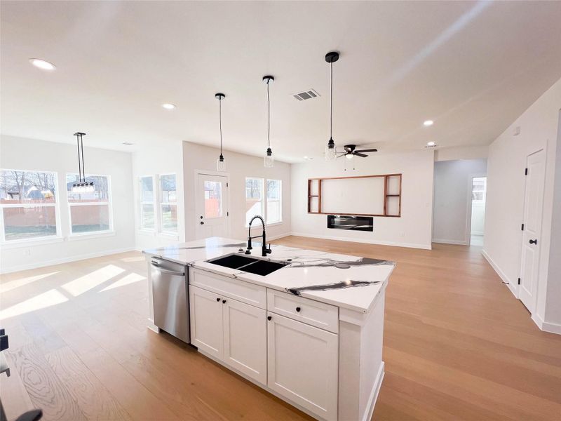 Kitchen featuring open floor plan, light wood-style flooring, white cabinetry, pendant lighting, and a kitchen island with sink