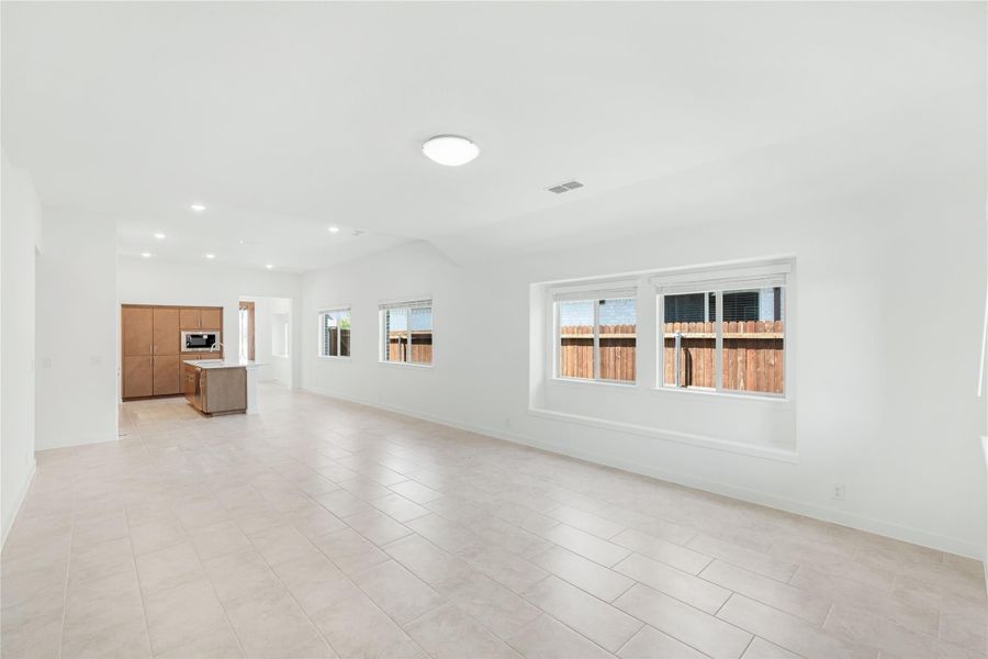 Open living area with tile floors and vaulted ceiling, open to kitchen with wood cabinets and island