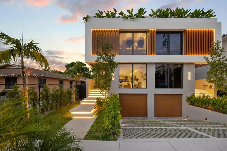 Modern multi-level exterior featuring clean-lined smooth stucco, vertical slat accents, dual garage doors with wood-finish surfacing, tiered concrete steps with integrated lighting, and a flat roofline with built-in perimeter planter boxes Modern multi-level exterior featuring clean-lined smooth stucco, vertical slat accents, dual garage doors with wood-finish surfacing, tiered concrete steps with integrated lighting, and a flat roofline with built-in perimeter planter boxes
