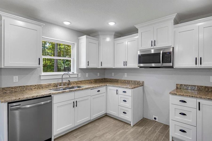 Kitchen featuring appliances with stainless steel finishes, white cabinets, wood tiled floors, light stone countertops, and recessed lighting Kitchen featuring appliances with stainless steel finishes, white cabinets, wood tiled floors, light stone countertops, and recessed lighting