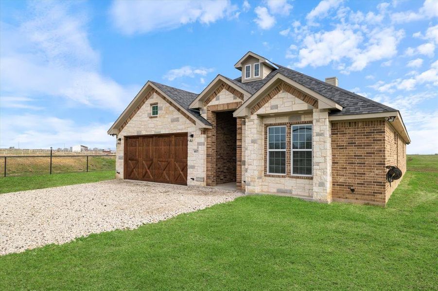 View of front facade featuring roof with shingles, brick siding, a front yard, a garage, and driveway