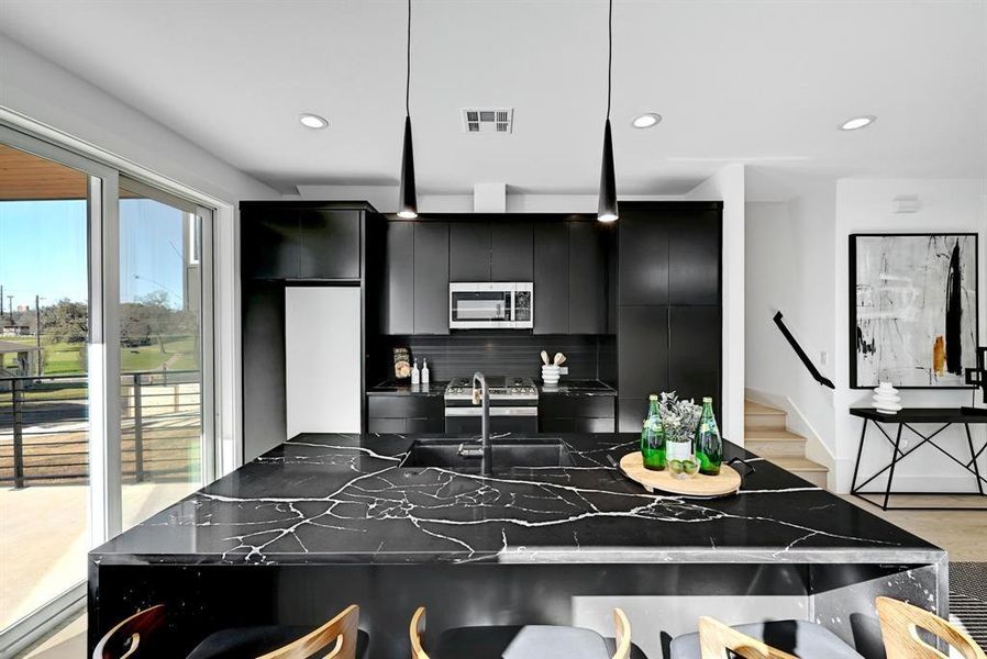 Kitchen with dark cabinetry, stainless steel microwave, decorative backsplash, a sink, and recessed lighting