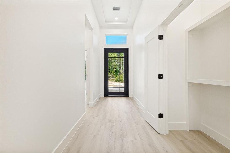 Foyer featuring light wood-finish flooring, a contemporary black paneled entry door with transom window, recessed lighting, and built-in shelving Foyer featuring light wood-finish flooring, a contemporary black paneled entry door with transom window, recessed lighting, and built-in shelving