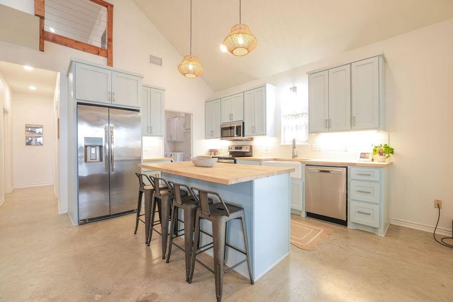 Kitchen featuring stainless steel appliances, a breakfast bar, decorative backsplash, high vaulted ceiling, and concrete floors
