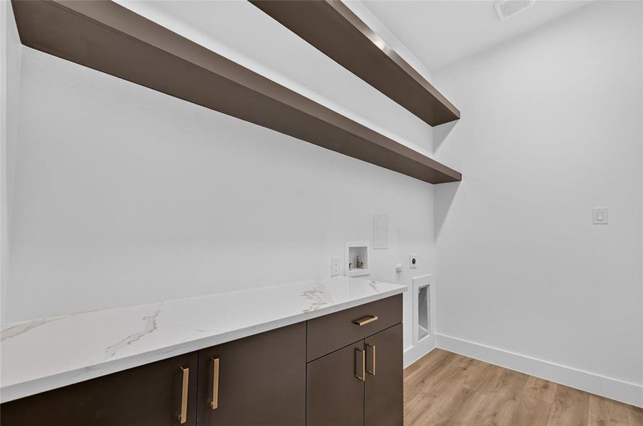 Laundry room featuring a white countertop with subtle veining, dark brown cabinetry with gold hardware, and two long floating shelves Laundry room featuring a white countertop with subtle veining, dark brown cabinetry with gold hardware, and two long floating shelves