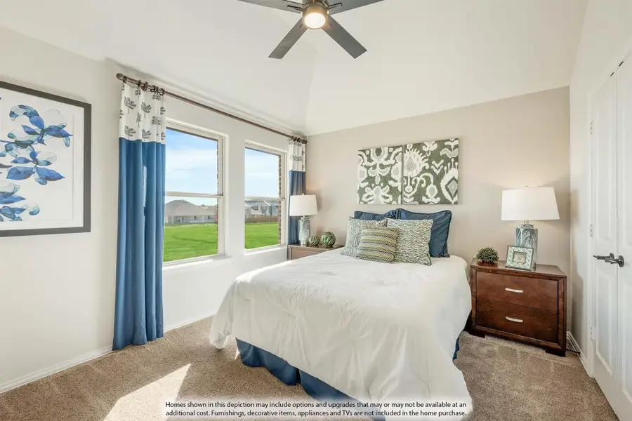 Bedroom with vaulted ceiling, ceiling fan, carpet flooring, and two windows with blue curtains overlooking a backyard