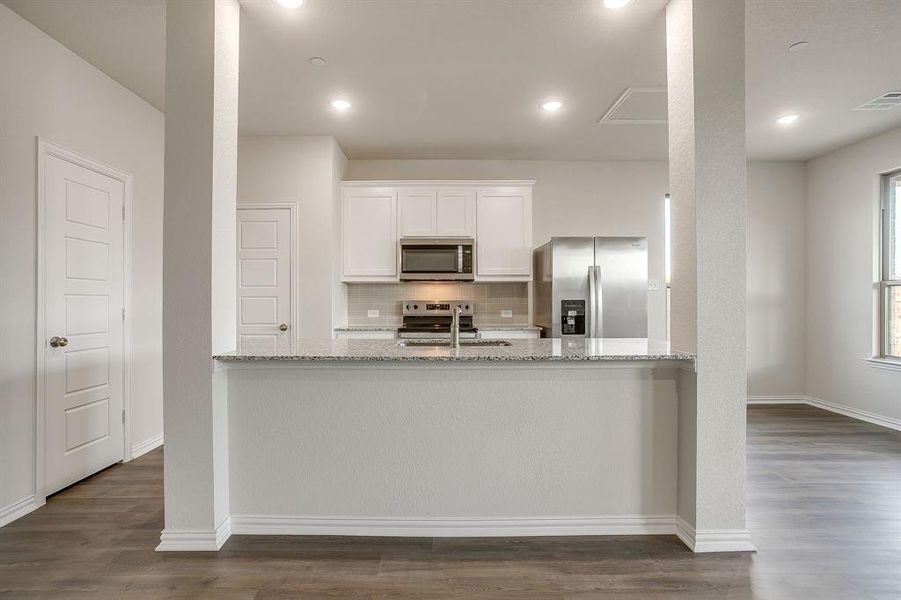 Kitchen with light stone countertops, white cabinets, decorative backsplash, stainless steel appliances, and dark wood-type flooring
