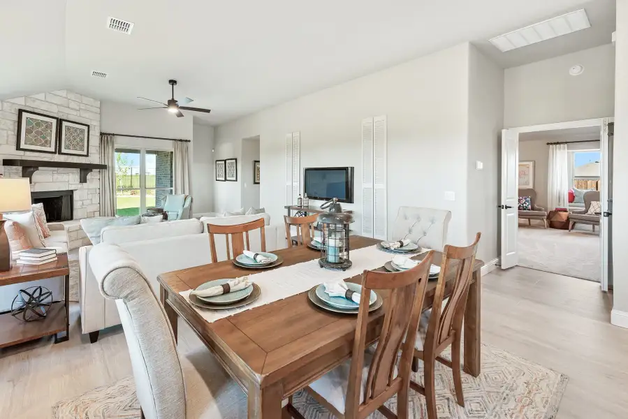 Open-concept dining area with wood table and chairs flowing into living room with stone fireplace and ceiling fan Open-concept dining area with wood table and chairs flowing into living room with stone fireplace and ceiling fan