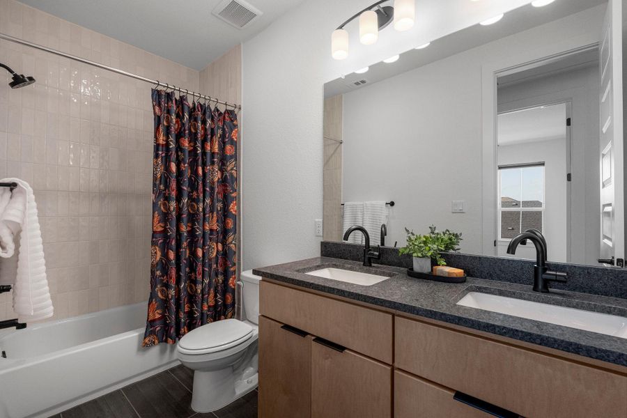Dual vanity with dark countertops complements the sleek, modern design of this full bathroom.