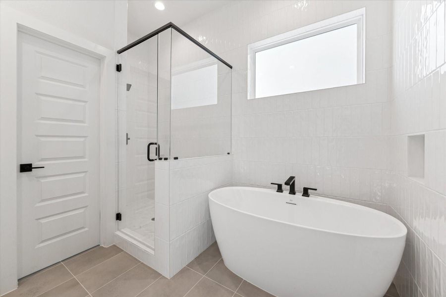 Primary bathroom features white tile, a soaking tub, and a glass-enclosed shower with a privacy barrier, creating a clean, spa-like retreat.