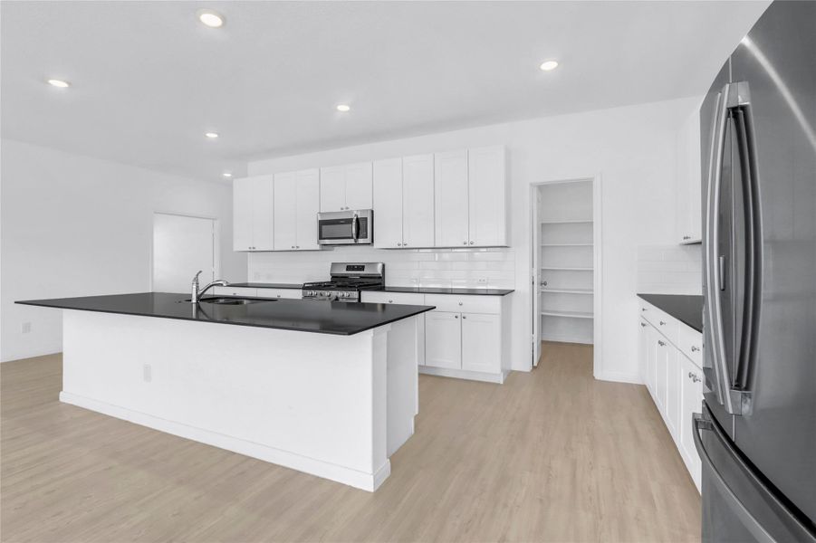 Kitchen with stainless steel appliances, an island with sink, white cabinets, backsplash, and light wood-style floors