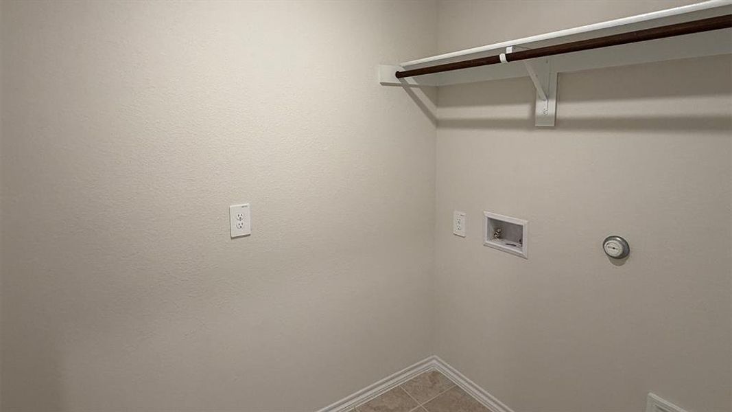 Dedicated laundry area featuring a tile floor, white baseboards, light neutral wall color, and a built-in hanging rod with shelving