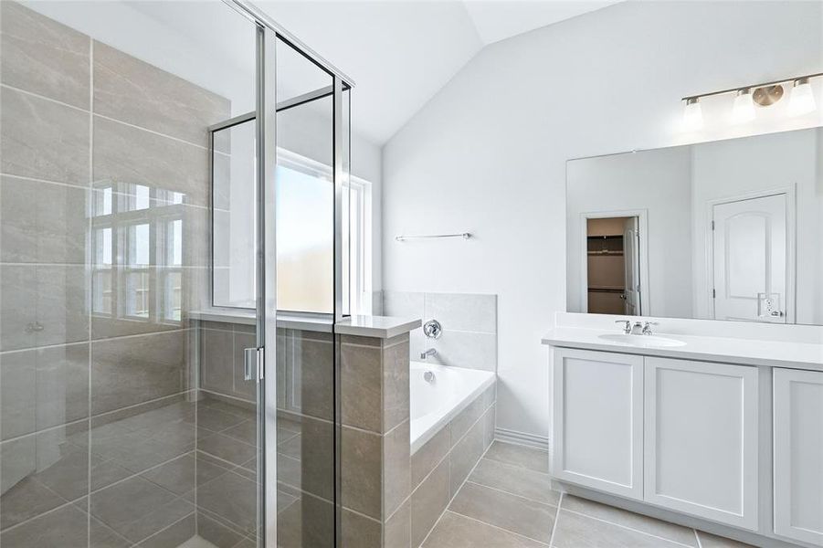 Bathroom featuring a shower stall, vanity, a garden tub, vaulted ceiling, and light tile patterned flooring Bathroom featuring a shower stall, vanity, a garden tub, vaulted ceiling, and light tile patterned flooring
