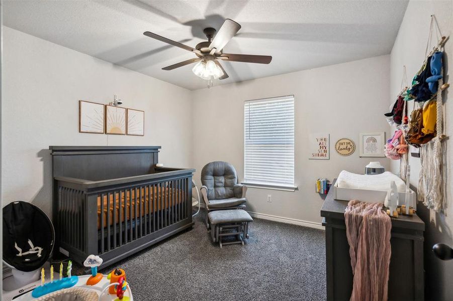 Carpeted bedroom featuring ceiling fan and a nursery area