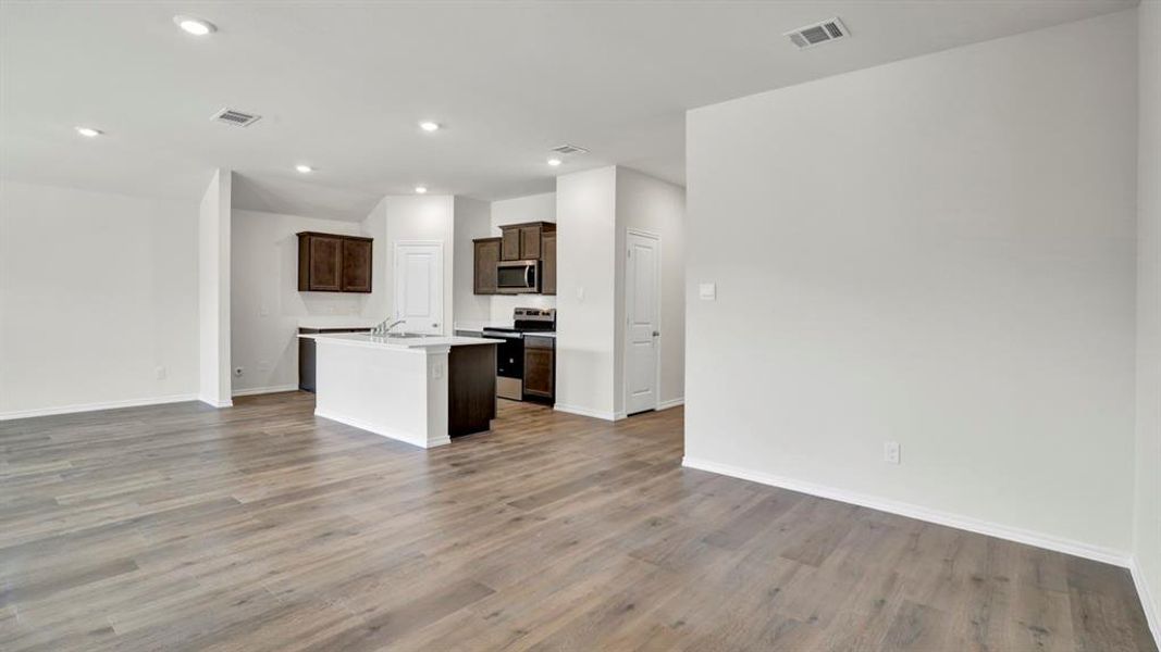 Open-concept living area featuring wood-finish flooring, recessed lighting, and a kitchen with dark wood cabinetry