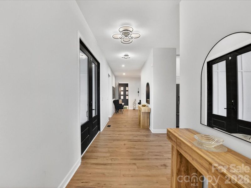 Bright, modern foyer with warm wood flooring, sleek black accents, and a long hallway leading into an inviting living space.