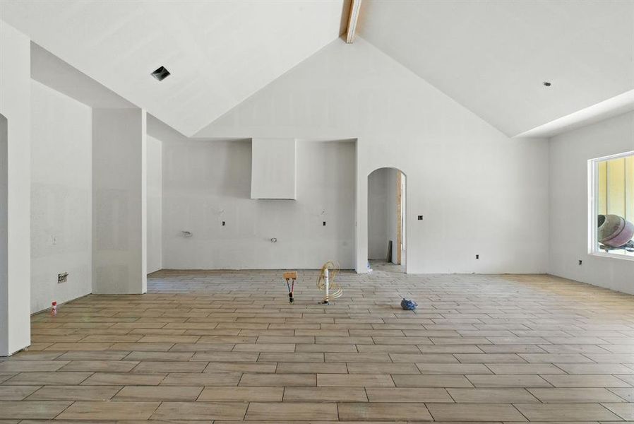 Unfurnished living room with beam ceiling, high vaulted ceiling, wood tiled floors, and arched walkways Unfurnished living room with beam ceiling, high vaulted ceiling, wood tiled floors, and arched walkways