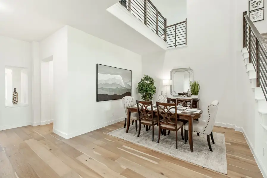 Formal dining room with two-story ceiling, wood dining table, six chairs, and light hardwood floors near staircase railing.