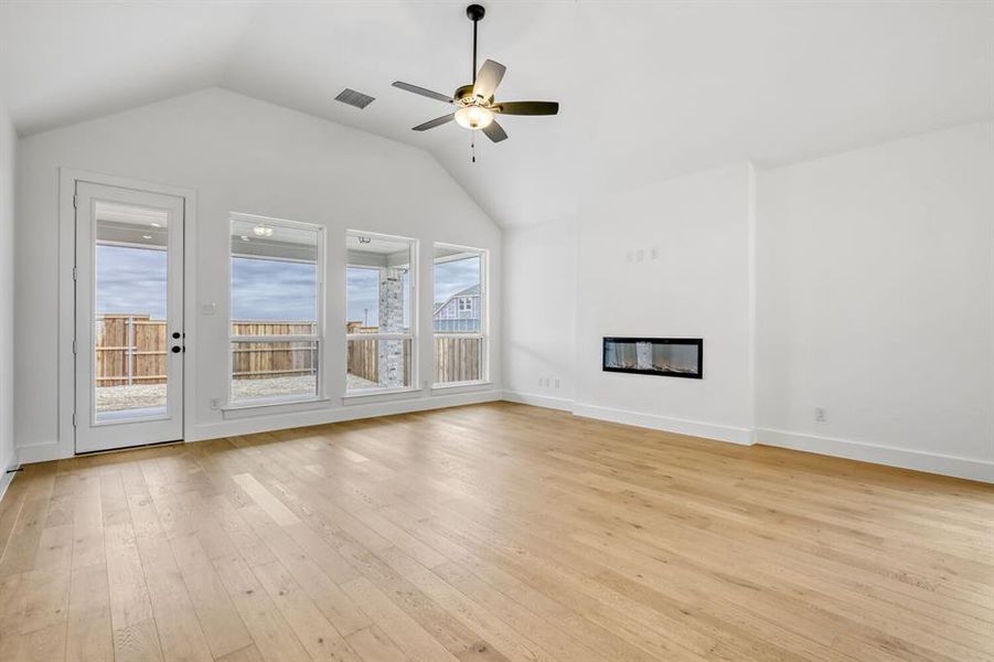 Unfurnished living room featuring ceiling fan, light wood finished floors, and a glass covered fireplace