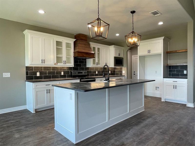 Kitchen with range hood, a center island with sink, sink, stove, and white cabinetry